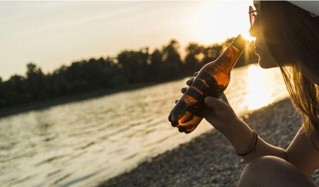 Eine Frau trinkt Malzbier bei Sonnenuntergang am See