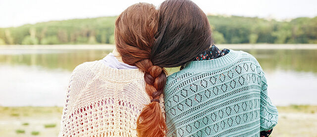Zwei Schwestern mit zusammengeflochtenem Haar, schauen zu einem See.