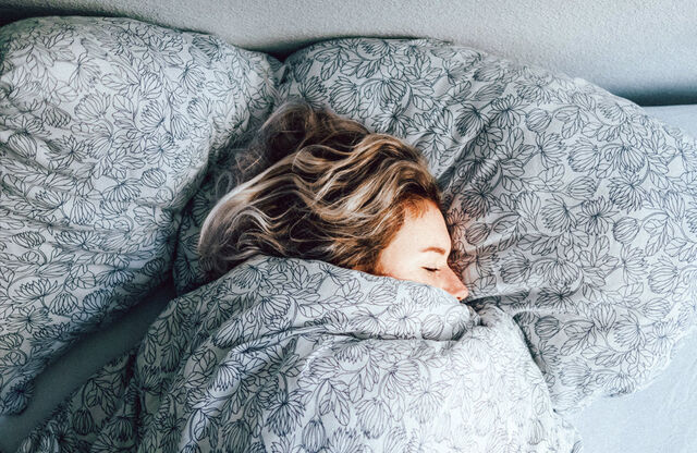 Eine Frau liegt zugedeckt im Bett und schläft.