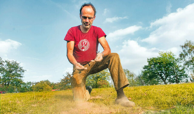 Bio-Bauer Ulf Allhoff-Cramer kniet auf seiner Weide und prüft den Zustand des Bodens. ﻿