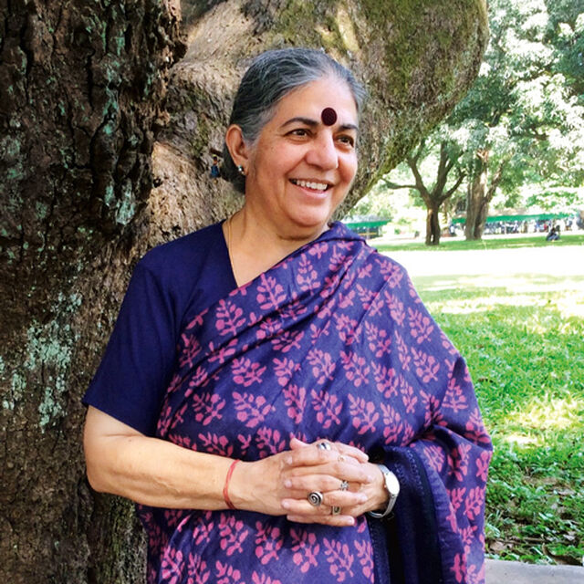 Vandana Shiva lehnt an einem Baum und lächelt