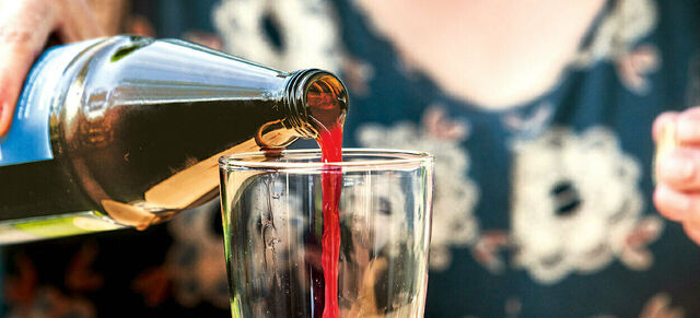 Aus einer Flasche wird rote Flüssigkeit in ein Glas gegossen