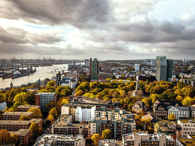 Hamburg von oben: Gebäude, Baumkronen, links die Elbe, wolkenverhangener Himmel