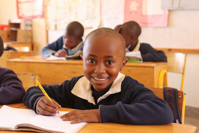 Ein Kind sitzt an einer Schulbank und lächelt in die Kamera
