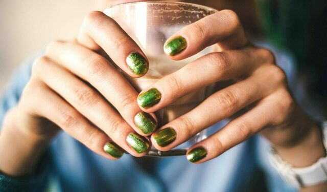 Zwei Frauenhände mit grün lackierten Nägeln halten ein Glas.