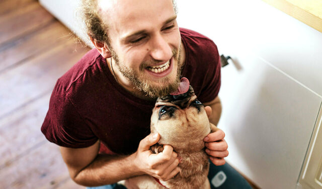 Junger Mann mit Bart kuschelt mit seinem Hund