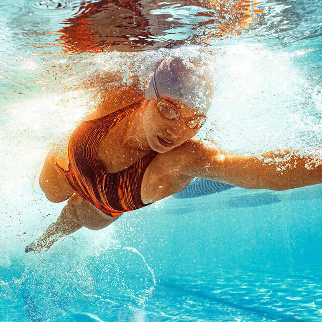 Eine Schwimmerin bei der Kraulbewegung. Ihr Kopf ist unter Wasser, ihren linken Arm streckt sie lang nach vorn.