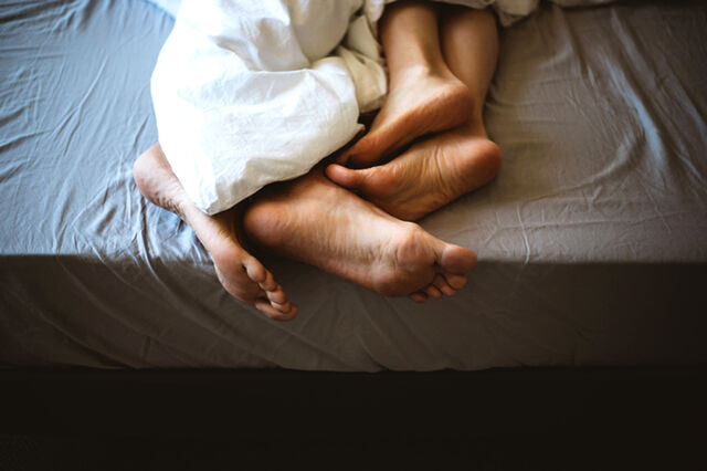 Die nackten Füße eines Paares schauen unter der Bettdecke hervor