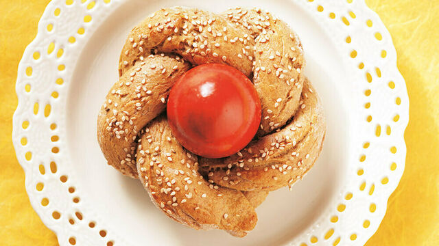 Ein Stück nestförmiges, mit Sesam bestreutes Hefegebäck, in dem ein rot gefärbtes Osterei sitzt
